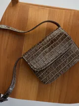 Mini cartera marrón con textura de cocodrilo, correa larga ajustable y cierre con solapa.