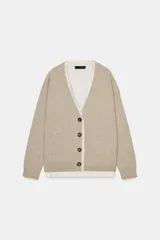 Chaqueta tipo cárdigan de lana en color beige, con diseño de tejido combinado que incluye una capa interior de tela clara. Presenta escote en pico, manga larga y cierre frontal con botones oscuros.