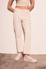 Pantalón de jean color crudo, corte flare, tiro medio y detalle de tachas plateadas en los laterales.