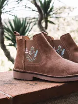Botin de cuero serraje color beige, con elastico lateral decorado con bordado floral multicolor y suela baja de goma.
