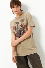 Remera color arena con estampado de serpiente y flores rojas, corte oversized y mangas cortas.