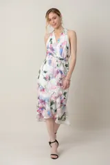 Vestido midi de gasa blanca con estampado floral en tonos rosados, azules y verdes. Presenta escote cruzado, espalda estilo halter, detalle de volados en la falda y corte irregular.