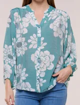 Blusa holgada de gasa texturizada color blanco con estampado de lunares negros, escote en V con botones frontales, mangas 3/4 abullonadas y puños elásticos.