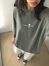 Remera oversize de color marrón topo con efecto acid wash, cuello redondo y manga corta. Cuenta con un pequeño estampado gráfico frontal con el texto 'WAKE UP IND' y una calavera.