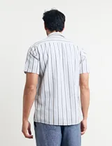 Camisa de manga corta con rayas verticales en tonos celeste, blanco, tostado y negro. Tiene cuello clásico, cierre con botones y bolsillo en el pecho.