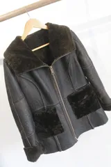 Campera reversible de cuero genuino y textura efecto corderito, color marrón oscuro, con cuello solapa ancho, cierre frontal y bolsillos delanteros amplios.