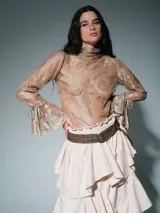 Polera de encaje transparente con cuello alto, mangas largas acampanadas con lazos ajustables en los puños y diseño floral.