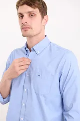 Camisa celeste con cuello abotonado, manga larga con puños abotonados y bolsillo en el pecho.