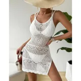 Vestido corto de playa color blanco, confeccionado en tejido calado con diseño geométrico y floral. Es de corte recto al cuerpo, sin mangas, con escote redondo y un tajo lateral.