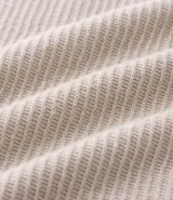 Polo de manga larga color beige claro, confeccionado en tejido texturizado (posiblemente acanalado o waffle). Presenta un cuello polo con escote profundo en V sin botones.