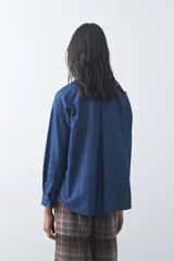Camisa de jean en tencel con silueta amplia, hombros caídos, cuello clásico y cierre frontal con botones. Presenta ruedo curvo con tajos laterales y pliegue en la espalda.