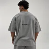 Remera oversize gris melange de algodón con elastano, de manga corta y cuello redondo. Presenta un pequeño bordado con la palabra 'MENTALITY' en la parte posterior.