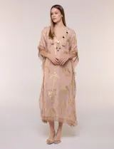 Vestido midi tipo túnica de silueta holgada, marca America & Beyond, color rosado con estampado metalizado dorado de palmeras. Cuenta con escote en V, detalles de borlas, espejos y apliques decorativos, y flecos en mangas, laterales y ruedo.