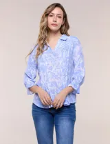 Blusa celeste con estampado efecto pincelada blanca, de corte semi holgado, escote en V con cuello solapa y media abotonadura frontal con botones nacarados. Presenta finas alforzas verticales en la pechera y mangas 3/4 con puños elastizados.