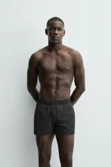 Short de baño negro de tejido técnico con estructura ripstop resistente a desgarros, cintura ajustable con cordón y bolsillos laterales.