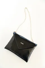 Sobre de mano tipo clutch confeccionado en charol negro brillante con solapa geométrica y cadena metálica plateada delgada.