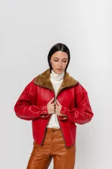 Chaqueta bomber de cuero color rojo con cuello de piel sintética color marrón, cierre frontal con cremallera, mangas largas y corte a la cintura.