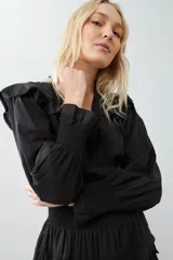 Vestido corto negro con escote en V, mangas largas abullonadas con puños elásticos, falda con volados y cinturón trenzado.