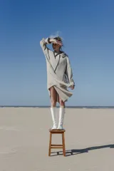 Tapado amplio color gris claro, confeccionado en lana fina sin teñir. Tiene hombros caídos, mangas largas con presillas y detalle de color en el cuello.