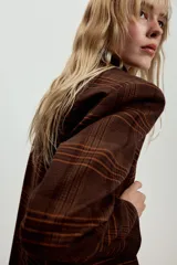 Blazer Zara de cuello solapa y manga larga, con estampado de cuadros en tonos marrones y rojizos. Presenta cierre frontal con dos botones y bolsillos delanteros con solapa.