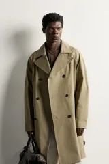 Trench regular fit de color beige, confeccionado en tejido técnico repelente al agua, con diseño de botonadura cruzada, cuello con solapas, mangas raglán con trabillas ajustables en los puños y cinturón del mismo tejido.