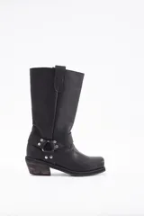 Bota de caña alta estilo western confeccionada en cuero vacuno negro. Presenta un diseño robusto con taco cuadrado de madera, punta redondeada y una tira decorativa con herrajes metálicos y tachas en la zona del tobillo.