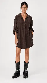 Vestido corto de estilo camisero con silueta amplia y fluida. Presenta cuello camisero, cierre frontal parcial con botones, mangas largas con detalle de ajuste y bolsillos laterales.