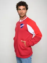Campera tipo bomber de felpa, color rojo con detalles en blanco en las mangas y cuello. Presenta cierre frontal completo, logo de Umbro y escudo del Club Nacional de Football bordados en el pecho.