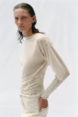 Jersey de punto semitransparente color crudo con cuello redondo y mangas largas, con detalles de nido de abeja elástico en el cuerpo y los puños.