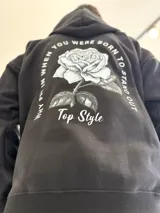 Canguro negro de corte oversize con capucha y gran estampa en la espalda de una rosa acompañada por la frase "Why fit in when you were born to stand out" y el texto "Top Style".