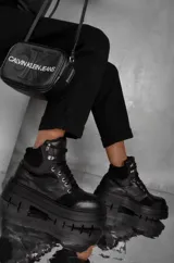 Borcegos de cuero vacuno color negro, con suela track de plataforma alta, cordones frontales con ganchos metálicos y combinación de texturas en cuero liso y gamuza.