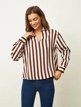 Blusa de color blanco con cuello en V y mangas largas con puños abotonados. Presenta un diseño de corte recto y holgado.