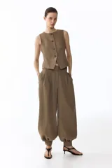 Pantalón de sarga de tiro alto, color marrón, con diseño de piernas globo, pinzas y puños abotonados con frunces. Cuenta con bolsillos laterales discretos y cierre frontal con botón y corchetes ocultos.