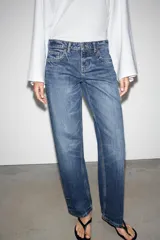 Jeans de mezclilla en color negro gastado, tiro bajo, corte de pernera recta y diseño clásico de cinco bolsillos con cierre frontal de cremallera y botón metálico.