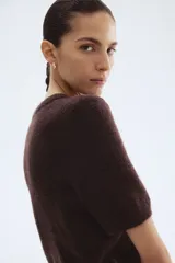 Buzo de punto fino color marrón oscuro, con cuello redondo y mangas cortas. Presenta remates acanalados en cuello, puños y bajo.