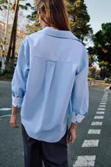 Camisa básica de algodón con cuello solapa, escote en pico y cierre frontal con botones. Presenta mangas largas con puños abotonados y bajo redondeado.