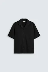 Camisa de corte regular fit confeccionada en tejido con estructura de color negro. Cuenta con cuello bowling, manga corta, aberturas laterales en el bajo y cierre frontal de botones.