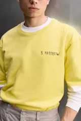 Camiseta de corte relaxed fit color amarillo, confeccionada en tejido compacto de algodón, con cuello redondo, manga corta y estampado frontal a contraste con texto y motivo floral pequeño.