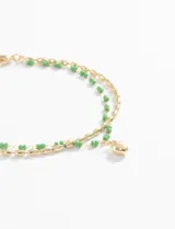 Pulsera dorada de doble cadena, una con cuentas verdes y otra con eslabones. Dije colgante de corazón dorado.