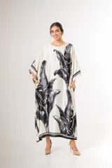 Maxi túnica oversize de tela con acabado nacarado, cuello redondo, mangas amplias y bolsillos laterales, con estampa de hojas de palmera en negro sobre fondo blanco.