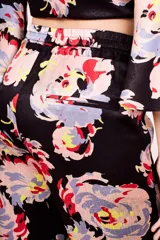 Pantalón negro con estampado floral multicolor, de corte acampanado y cintura elástica con cordón ajustable.