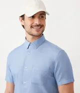 Camisa azul de manga corta con cuello clásico, corte slim fit, cierre frontal con botones blancos y bolsillo de parche en el pecho.