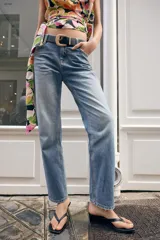 Jeans de tiro medio con corte slim fit, confeccionados en denim azul clásico. Presentan diseño de cinco bolsillos, cierre frontal con cremallera y botón, e incluyen un cinturón negro con hebilla metálica.