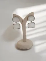 Caravanas colgantes de diseño geométrico con dos piezas rectangulares de acabado tipo nácar enmarcadas en metal plateado.