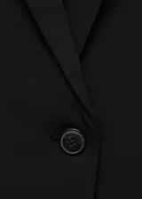 Blazer negro de corte entallado con hombros estructurados, cuello de pico con solapas de muesca, cierre delantero de un botón y bolsillos con solapa.