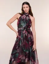 Vestido largo sin mangas de la marca RM Richards, con cuello alto halter y diseño asimétrico. Presenta un estampado floral en tonos bordó, verde y rosado sobre base satinada, con lazo ajustable en la cintura y falda fluida con capas asimétricas.