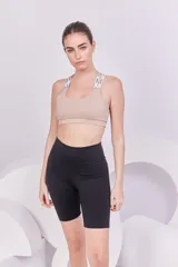 Top deportivo color beige con espalda cruzada, elástico en la base y tiras regulables con logo de la marca.