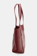 Bolso tipo shopper mini de color rojo oscuro o borgoña, con doble asa de hombro y pespuntes visibles. Cierre principal con botón imantado y bolsillo interior con cremallera.