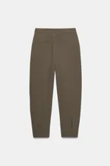 Pantalón de tiro medio con pinzas delanteras, bolsillos laterales y falsos bolsillos de vivo en la parte trasera. Presenta un corte holgado que se estrecha hacia el tobillo, con bajo acabado en pliegues y cierre frontal con cremallera, botón interior y gancho.