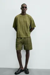 Camiseta de algodón de corte relajado (relaxed fit) con cuello redondo y manga corta. Presenta un tejido acanalado vertical (canalé) y un acabado ligeramente desgastado o lavado en tono verde oliva.